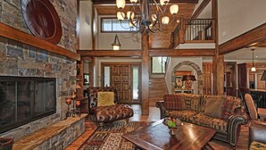 A spacious living room with a stone fireplace, leather sofa, and a large wooden coffee table. - Beautiful Sunriver Lodge Home steps to the Deschutes (Sunriver)