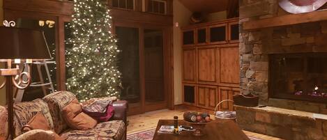 A cozy living room with a large Christmas tree, leather sofas, a wooden coffee table, and a stone fireplace.