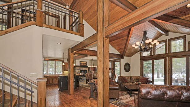 A spacious living area with a high ceiling, wooden beams, a staircase, and a view of the outdoors through large windows. - Beautiful Sunriver Lodge Home steps to the Deschutes (Sunriver)