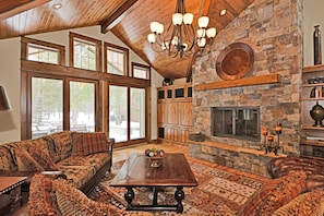A spacious living area with a stone fireplace, large windows, and a cozy seating arrangement. - Beautiful Sunriver Lodge Home steps to the Deschutes (Sunriver)
