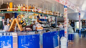 A bar area with shelves stocked with various liquor bottles, a counter with a drink dispenser, and a menu board displaying food items.