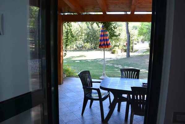 An outdoor patio with a table and chairs, a colorful umbrella, and a view of a garden.