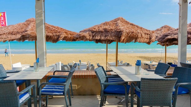 A beachside restaurant with thatched umbrellas, tables, and chairs facing the ocean.