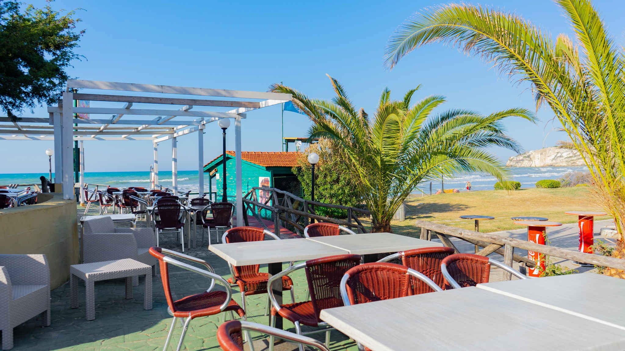 Un área de estar al aire libre con mesas y sillas, con vista a la playa y al océano.