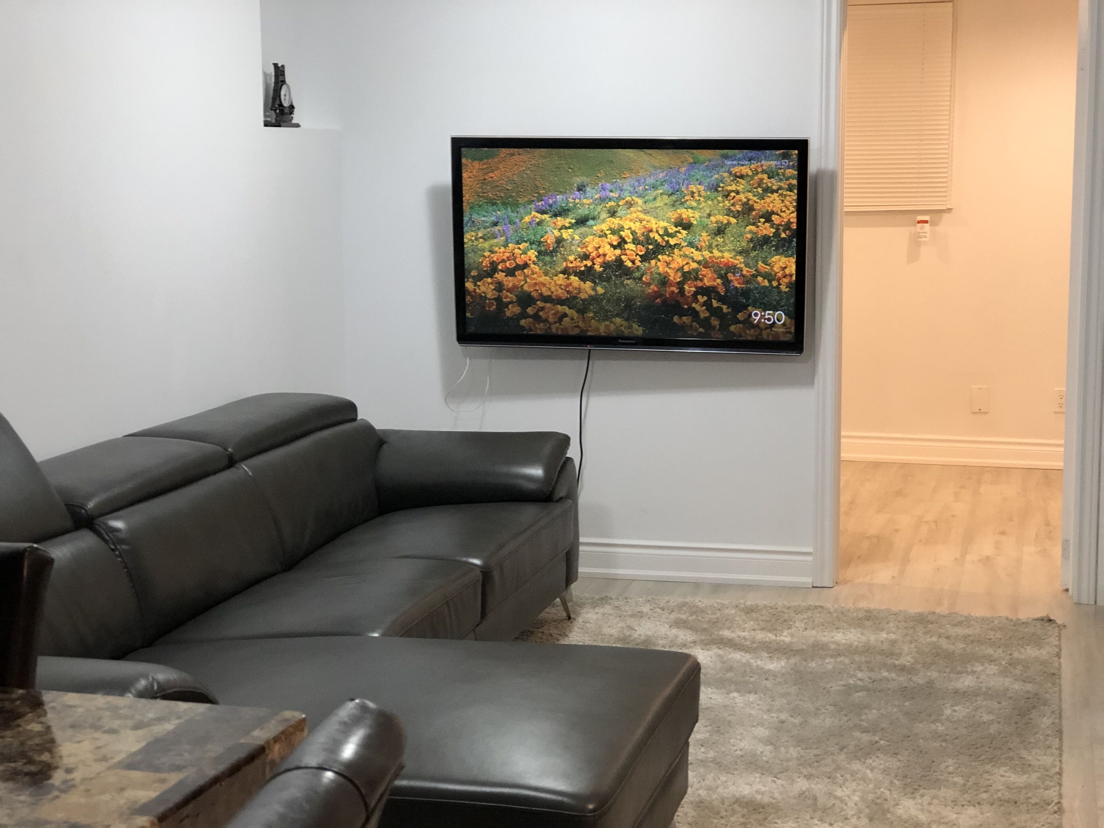 A living room with a gray sectional sofa, a flat-screen TV mounted on the wall, and a wooden floor.