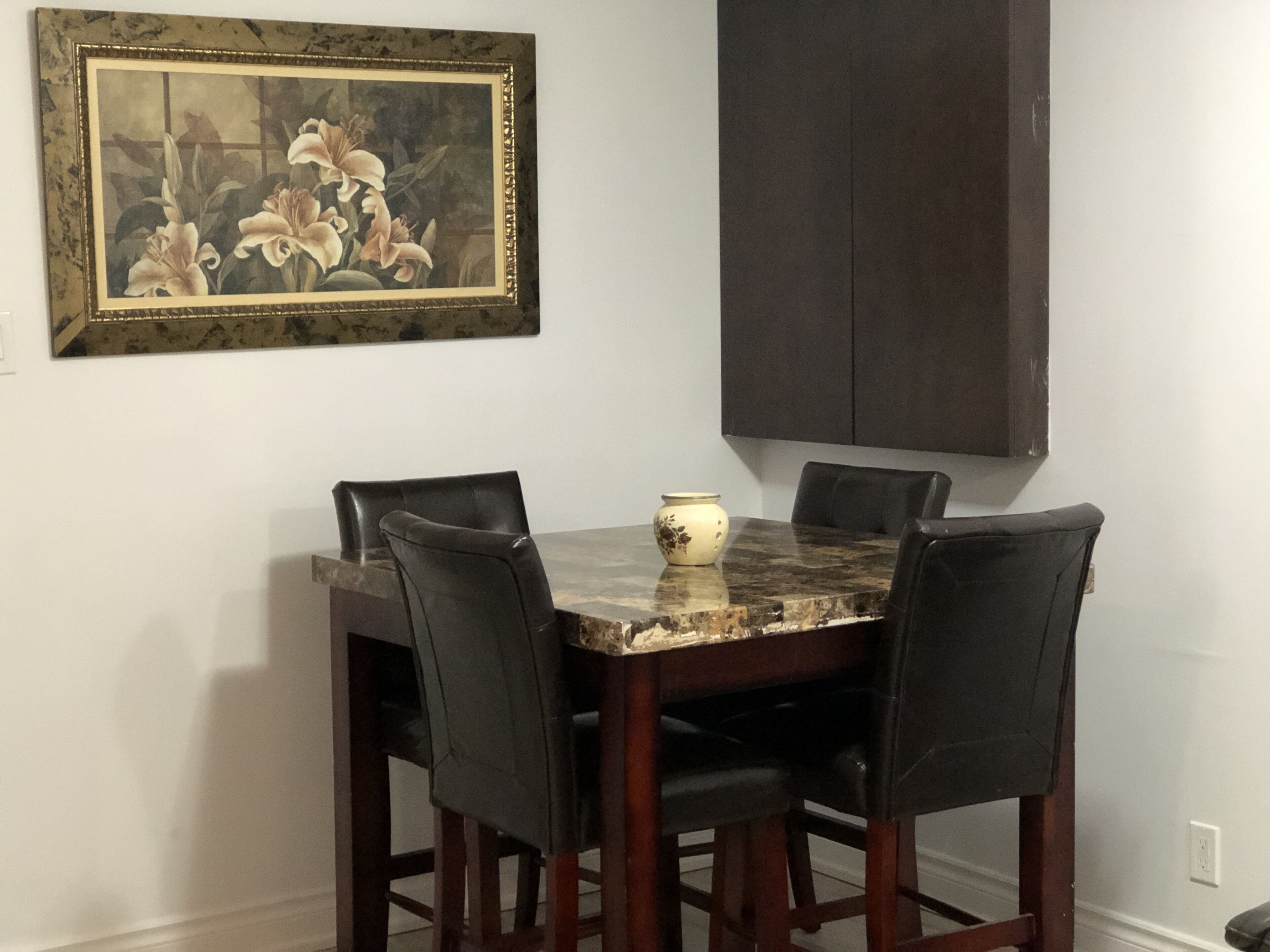 Une table à manger avec quatre chaises, un vase et un tableau encadré accroché au mur.