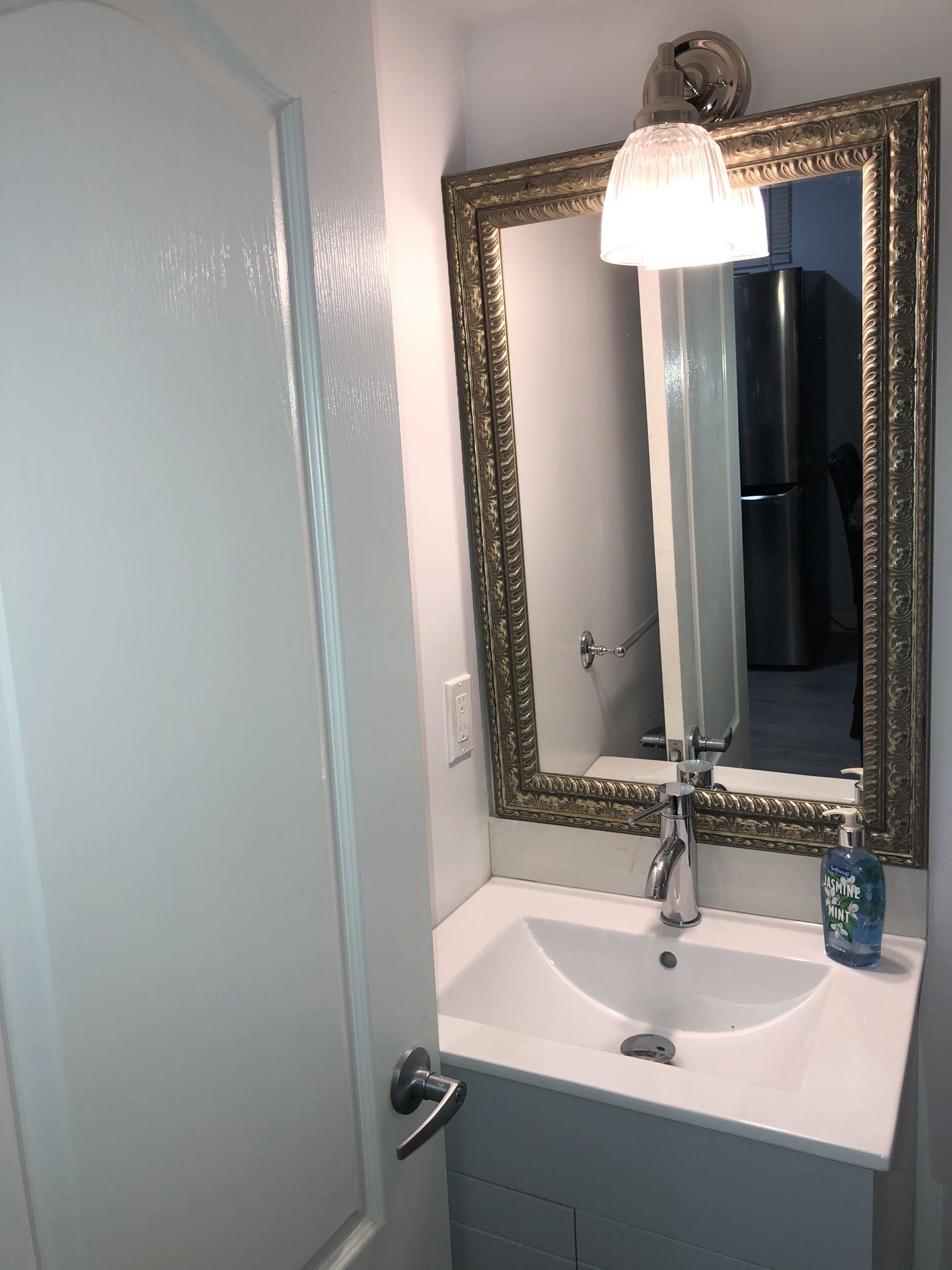 Een badkamer met een witte wastafel, een spiegel met een decoratief frame en een lamp boven de spiegel.