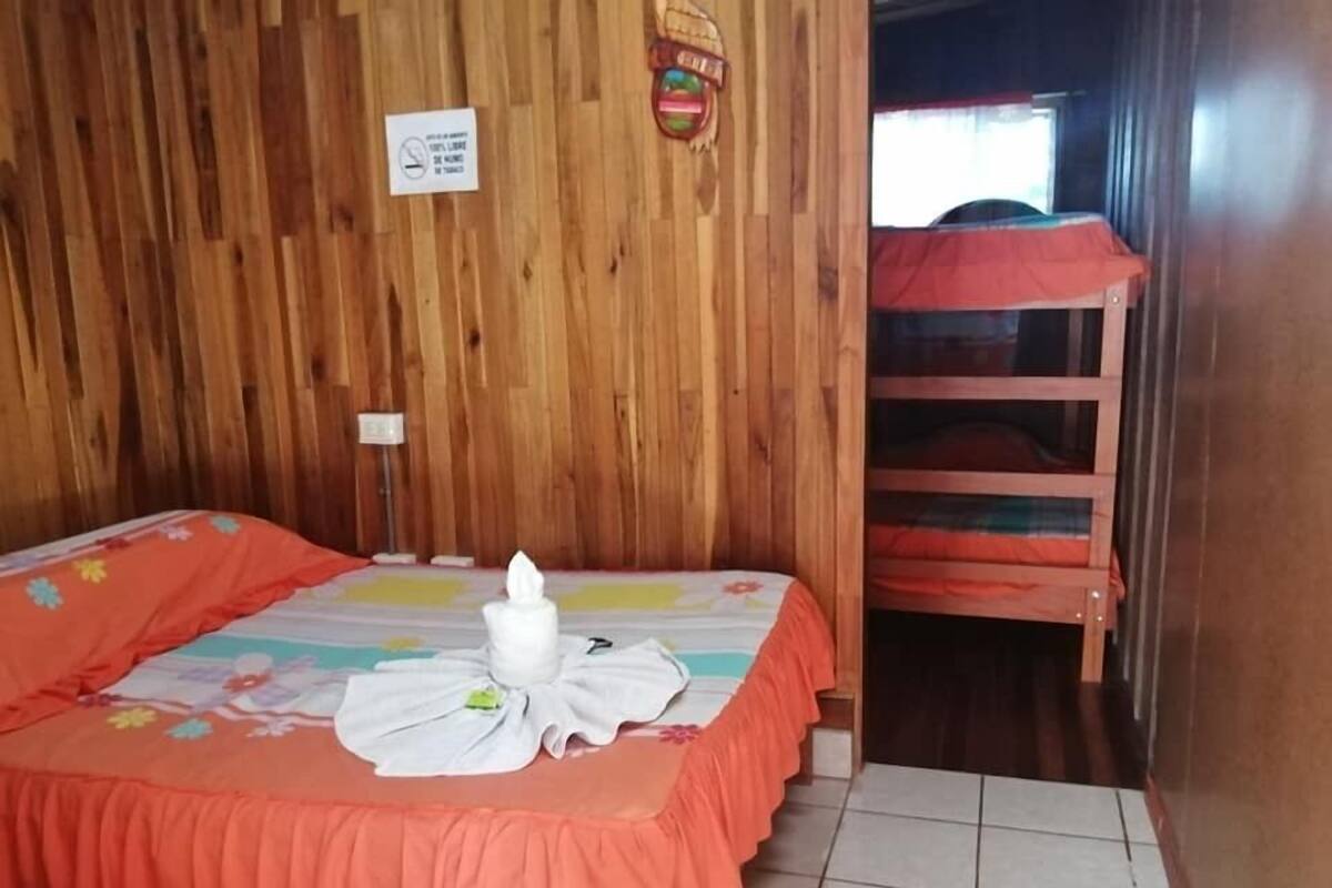Ein Zimmer mit einer Holzwand, einem Bett mit floralem Überwurf, einem weißen Handtuch auf dem Bett und einem Hochbett im Hintergrund.