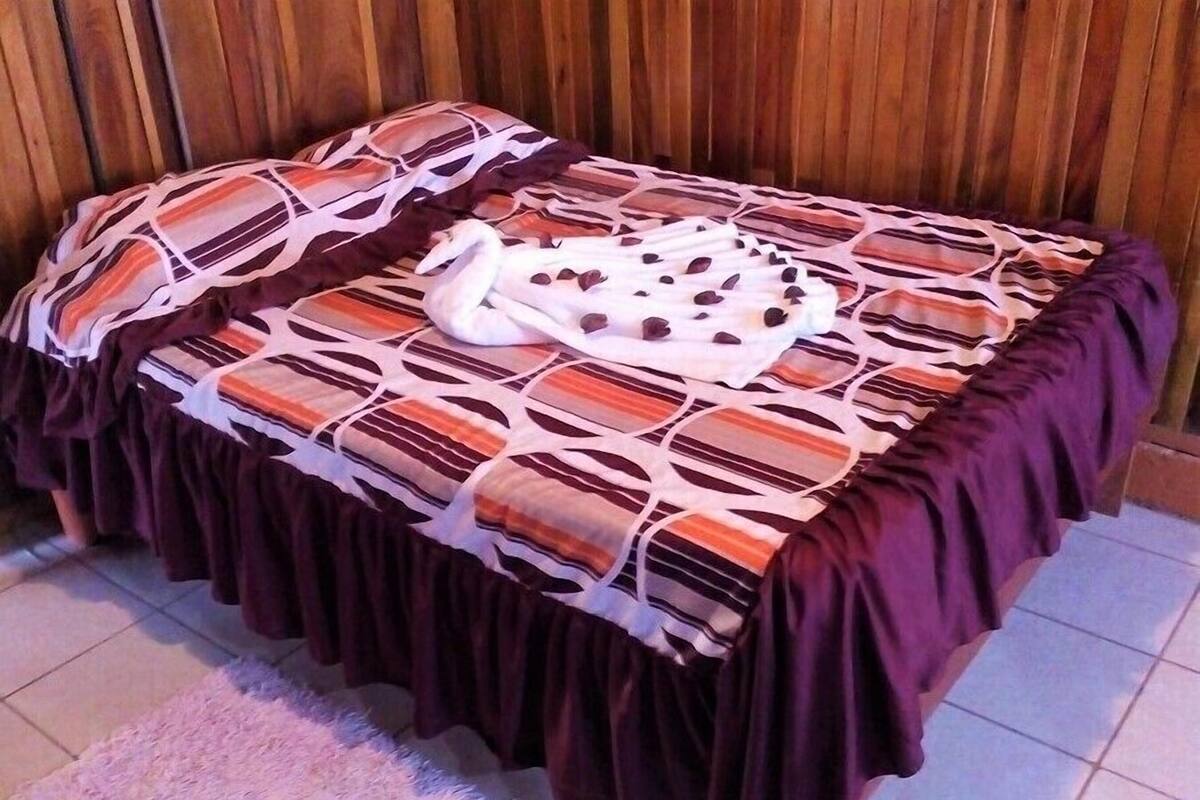 Ein Bett mit gemustertem Bettbezug und Kissen, ein dunkler Tisch mit Rock und ein flauschiger Teppich.