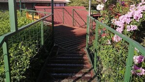 Un escalier avec des rampes en métal menant à un bâtiment doté d’un toit rouge.