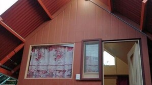 Une maison en bois avec un toit en pente, une fenêtre ornée de rideaux à motifs floraux et une clôture décorative avec des motifs de feuilles.