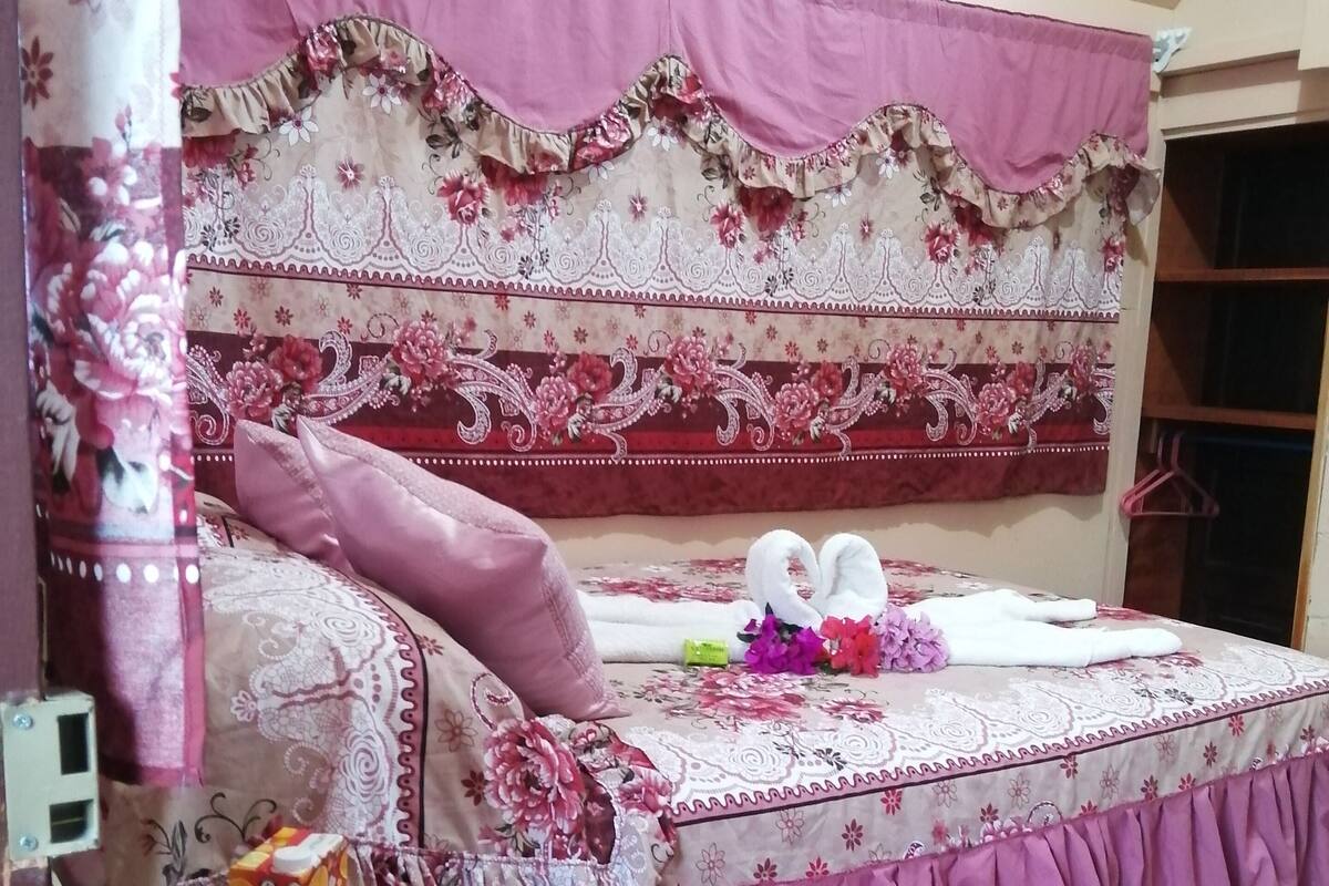 Ein Schlafzimmer mit einem blumengemusterten Bettüberwurf, einem Holznachttisch und einem Beistelltisch mit einem Glas.