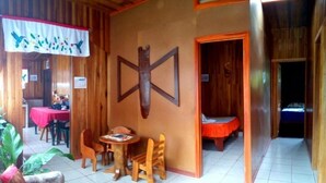 Une pièce chaleureuse avec une croix en bois accrochée au mur, un coin repas avec une nappe rouge et un lit recouvert d’une couverture rouge.