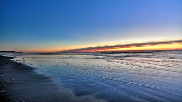 Una playa con mar tranquilo y cielo despejado durante el atardecer.