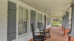 A covered porch with white siding and dark shutters, featuring two rocking chairs and a brick column. - Charming Southern Bungalow Convenient to Savannah (Bloomingdale)