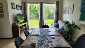 A dining area with a table set for two, a television on a stand, and a view of a garden through the window. - Playa Bejuco 3-bdrm home in beachfront condominium (Playa Bejuco)