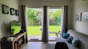 A living room with a TV, sofa, and a sliding glass door leading to a garden. - Playa Bejuco 3-bdrm home in beachfront condominium (Playa Bejuco)