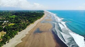 An aerial view of a beach with a long stretch of sand, waves, and a clear sky.