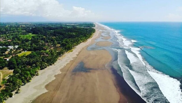 An aerial view of a beach with a long stretch of sand, waves, and a clear sky. - Playa Bejuco 3-bdrm home in beachfront condominium (Playa Bejuco)