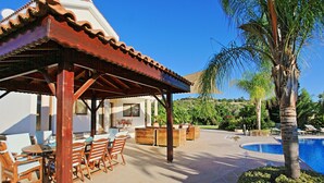 A covered outdoor seating area with wooden furniture, a pool, and a palm tree. - Skouli: A traditional property in Skoulli, near Polis, with heated pool (Polis)