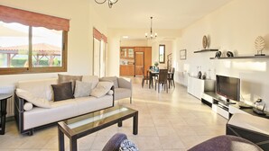 A spacious living room with a sofa, coffee table, and TV. There is a dining area with chairs and a table. The room has a large window and a chandelier. - Skouli: A traditional property in Skoulli, near Polis, with heated pool (Polis)