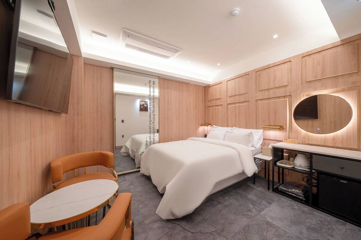 A modern hotel room with a bed, a desk, a chair, and a TV.
