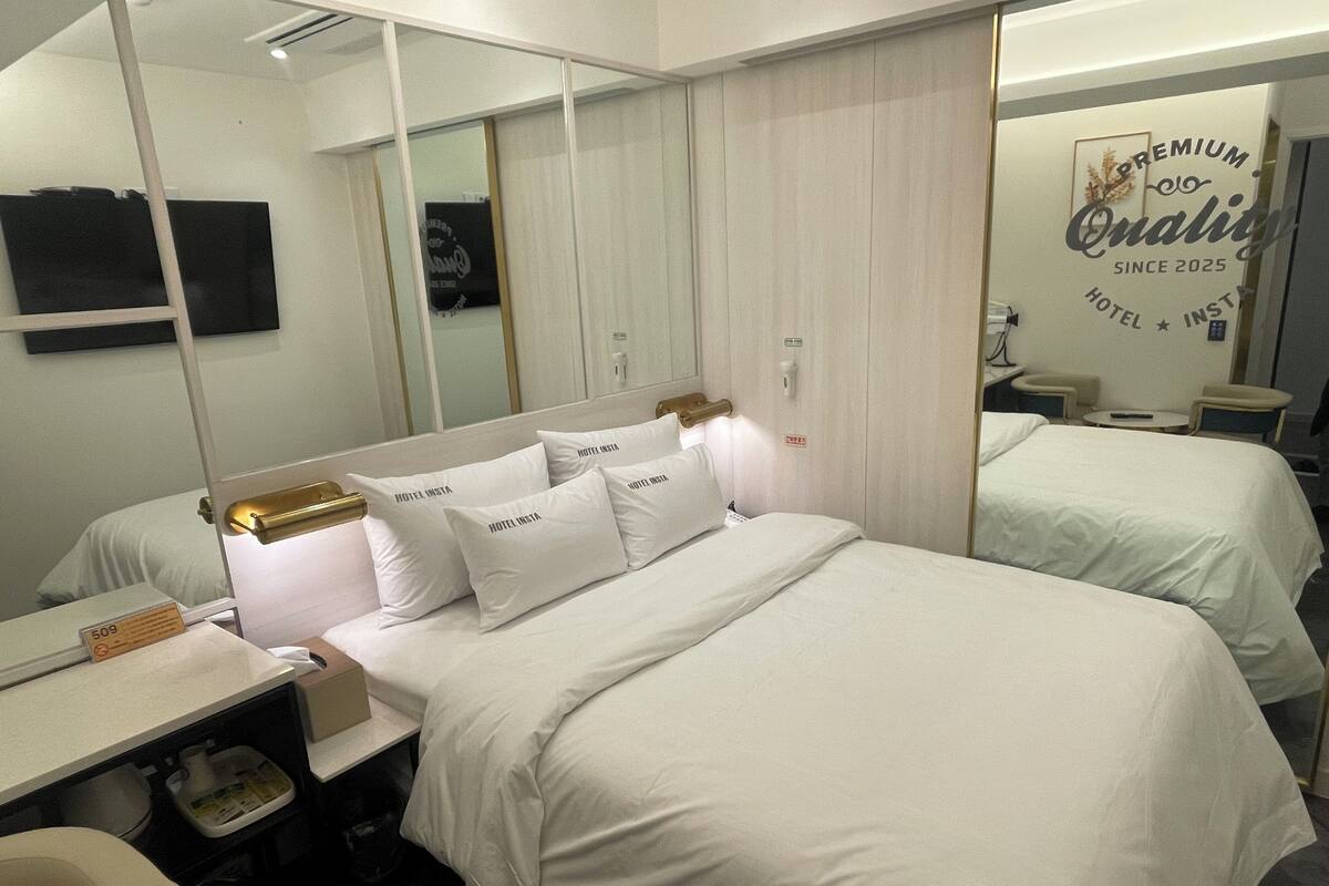 A hotel room with a large bed, a bedside table, a chair, a desk, a mirror, and a wall with a sign.