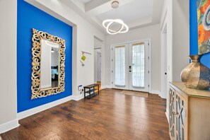 A spacious hallway with hardwood flooring, a large ornate mirror, and a modern light fixture.