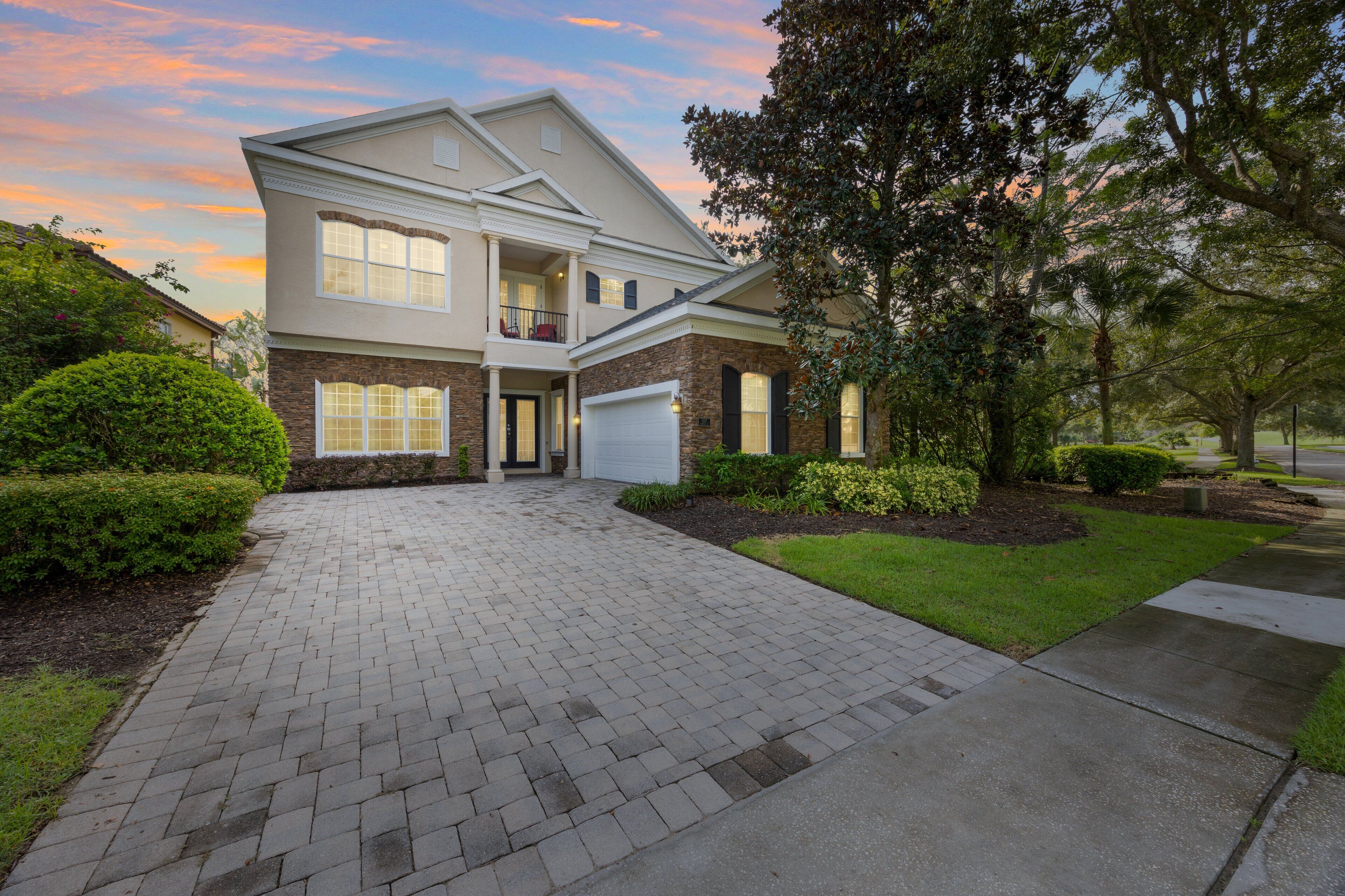A two-story house with a front garage, a landscaped driveway, and mature trees.