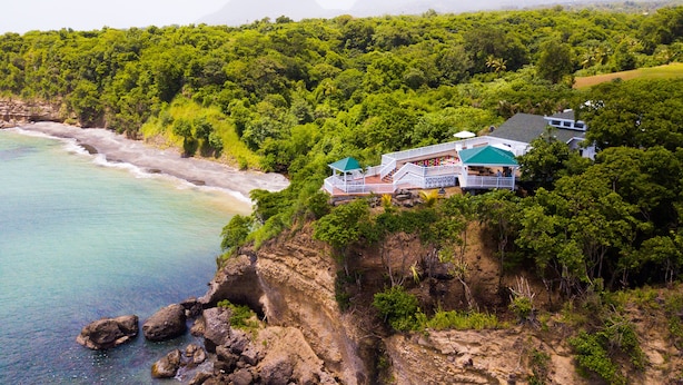 Uma propriedade costeira com uma casa grande, varanda e terraço, cercada por vegetação densa e com vista para a praia.