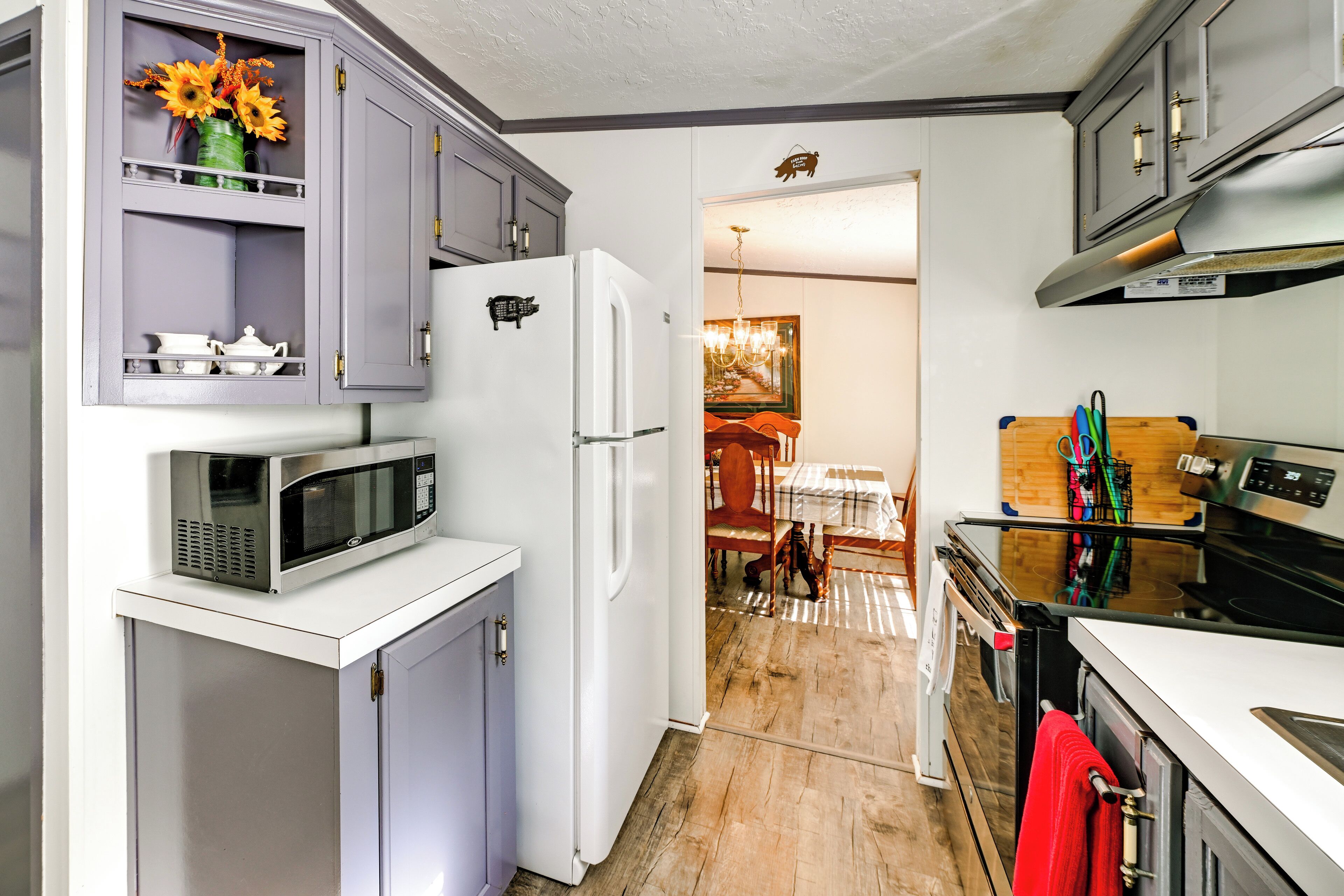 Een kleine keuken met een koelkast, magnetron en oven. In de aangrenzende eethoek staat een houten eettafel met stoelen.