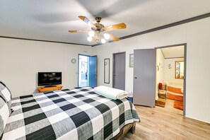 Ein Schlafzimmer mit einem Bett, einem Deckenventilator, einem Fernseher und einer Tür zu einem Badezimmer.