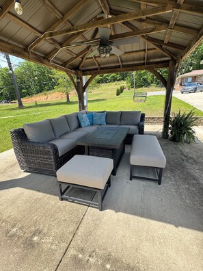 A covered outdoor seating area with a sectional sofa, two ottomans, and a table.