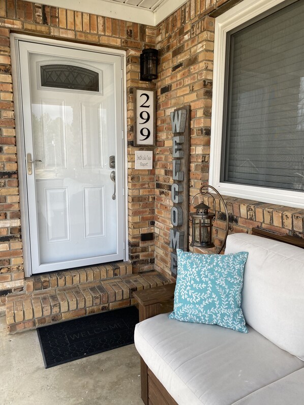 A brick exterior with a white door, a welcome sign, and a number sign indicating the address.