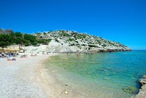 A beach with clear water, people sunbathing, and a rocky hill in the background. - VILLA FAR- 15 MIN WALK TO THE BEACH (Puerto Pollensa)