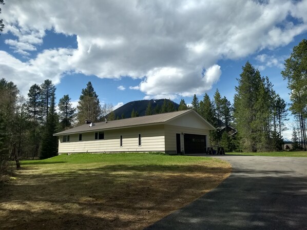 A single-story building with a garage, surrounded by a grassy area and tall trees, under a partly cloudy sky.