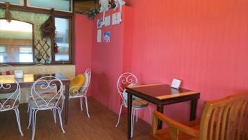 A dining area with a wooden table and metal chairs, a red wall, and a window with a view.