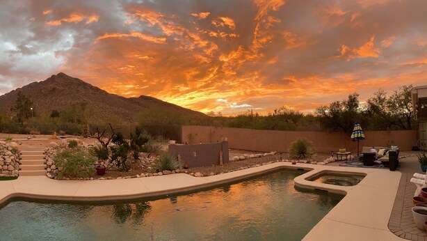 Ein Garten mit Swimmingpool, Liegestühlen und einem Bergpanorama bei Sonnenuntergang.