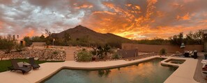 Patio con piscina, sillas de descanso y montañas al atardecer.