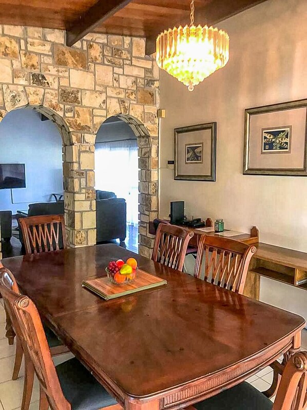 A dining area with a wooden table, chairs, a chandelier, stone walls, and framed artwork.