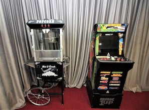 A popcorn machine and an arcade game labeled 'Arcade 1UP' in front of a curtain backdrop. - Red Corvette House with Theater Room - WR001 (Davenport)