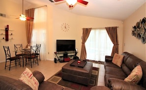 A living room with a sofa set, a television, a dining area with chairs and a table, and a ceiling fan. - Red Corvette House with Theater Room - WR001 (Davenport)