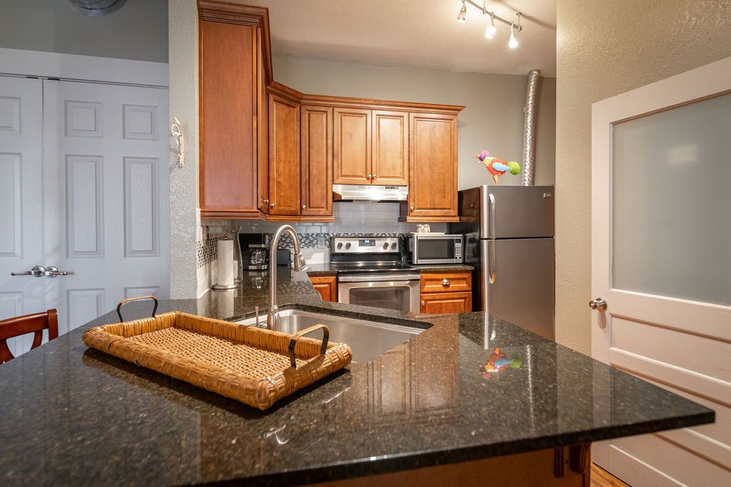 A kitchen with granite countertops, wooden cabinets, stainless steel appliances, and a woven basket on the counter.