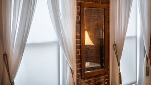 Una habitación con pared de ladrillo, espejo con marco de madera y cortinas blancas.