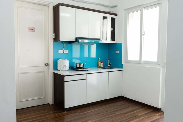 Compact kitchen with white cabinetry, electric kettle, and stove, adjacent to a temperature-controlled door and a window.