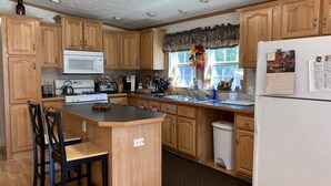 A kitchen with wooden cabinets, a microwave, stove, and a refrigerator. There is a window with a curtain and a calendar on the wall. - Log Cabin Near Hunter Mountain (Hunter)