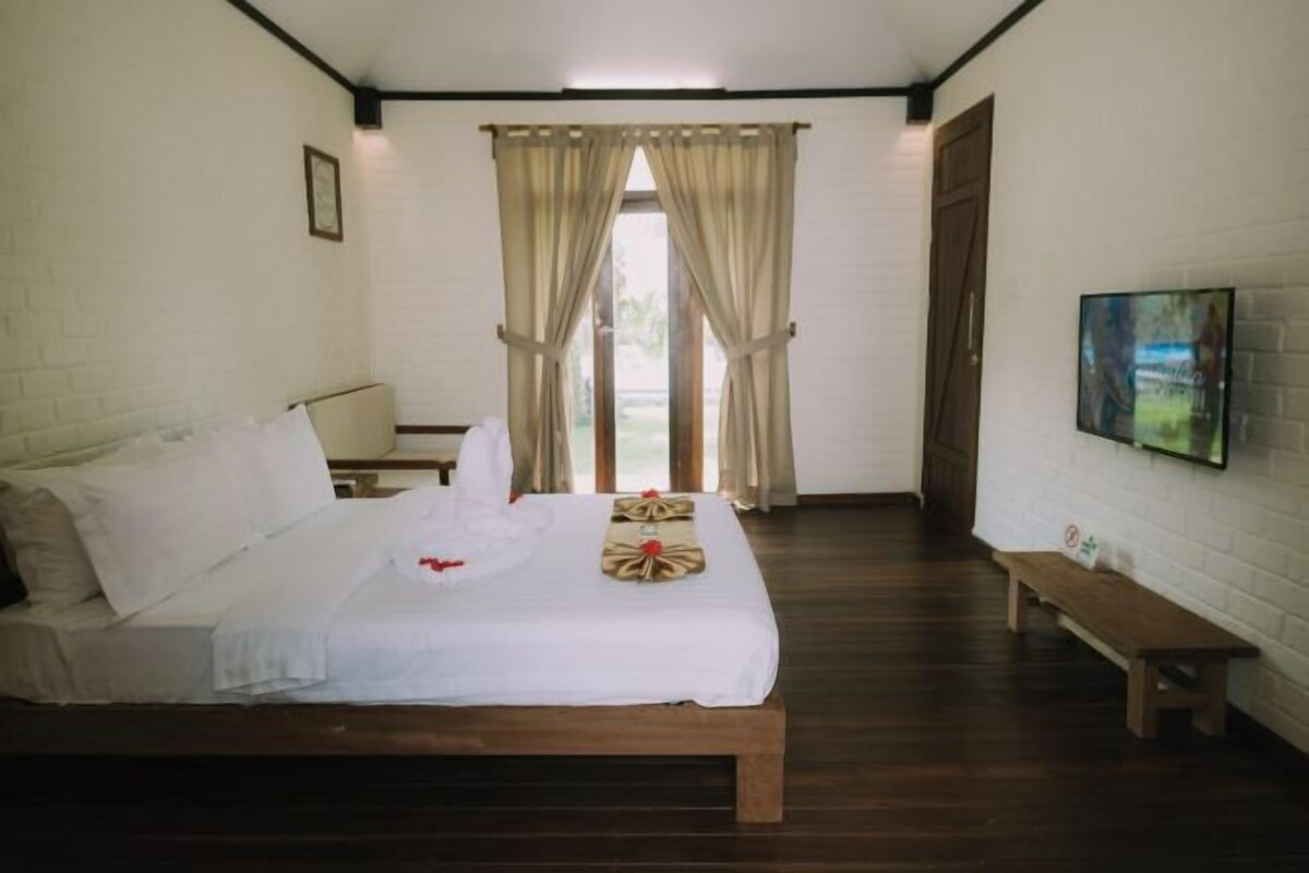 A hotel room with a bed, a bench, a TV, and a window with curtains.