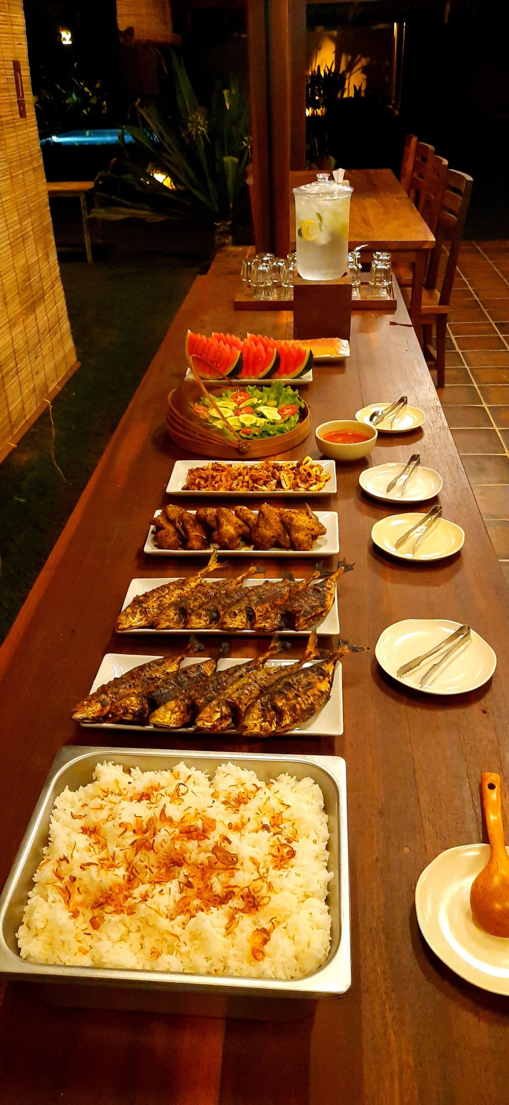 Ein reichhaltiges Buffet mit verschiedenen Speisen, darunter Reis, frittiertem Fisch und Salaten.