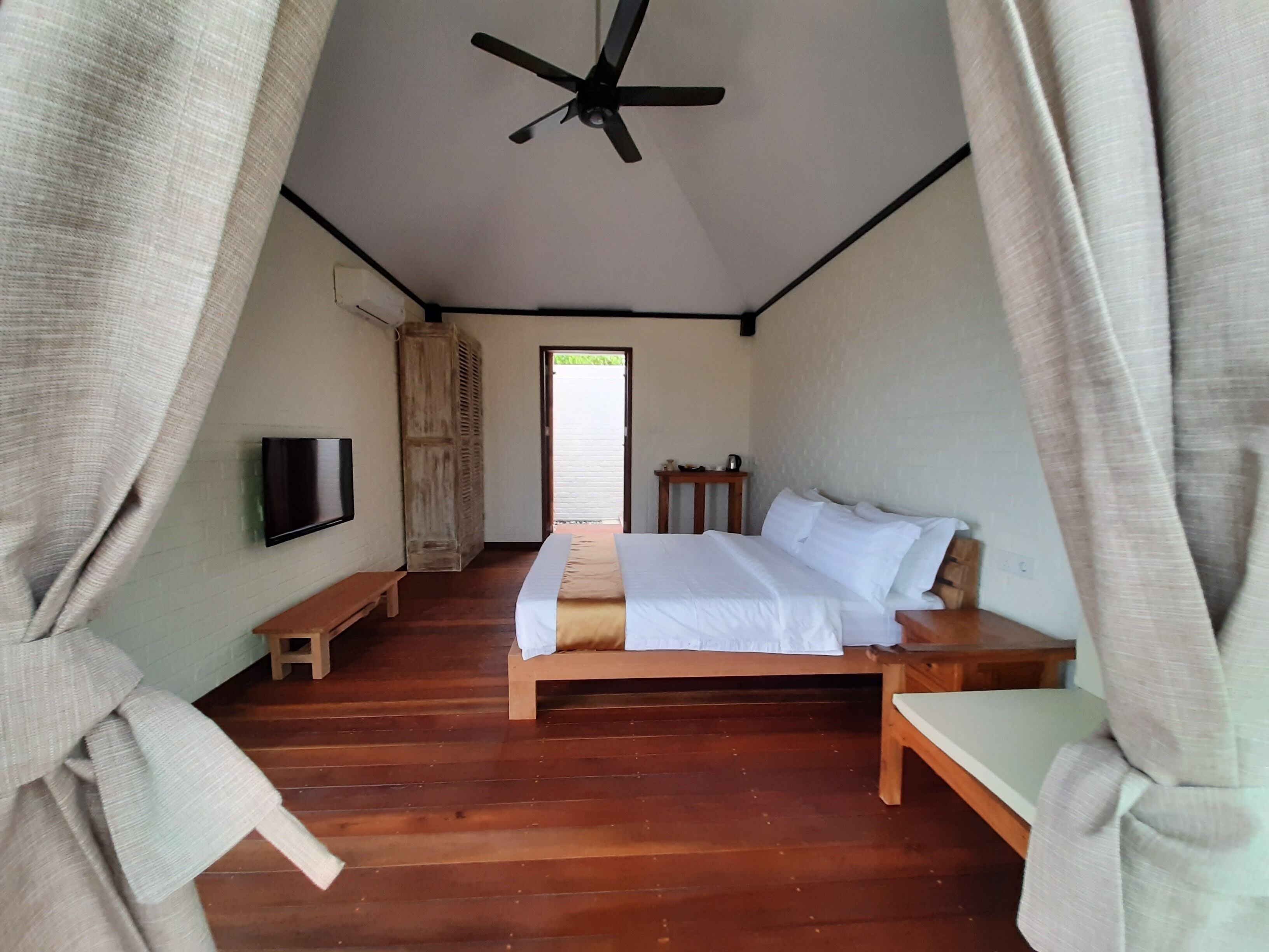 Un dormitorio con cama, televisión, banca de madera y ventilador de techo.