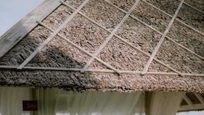 A thatched-roof structure with white drapery and wooden chairs. - The Kelong Trikora Resort (Bintan)